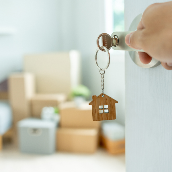 Une personne tenant une clé de maison avec un porte-clés en forme de maison.