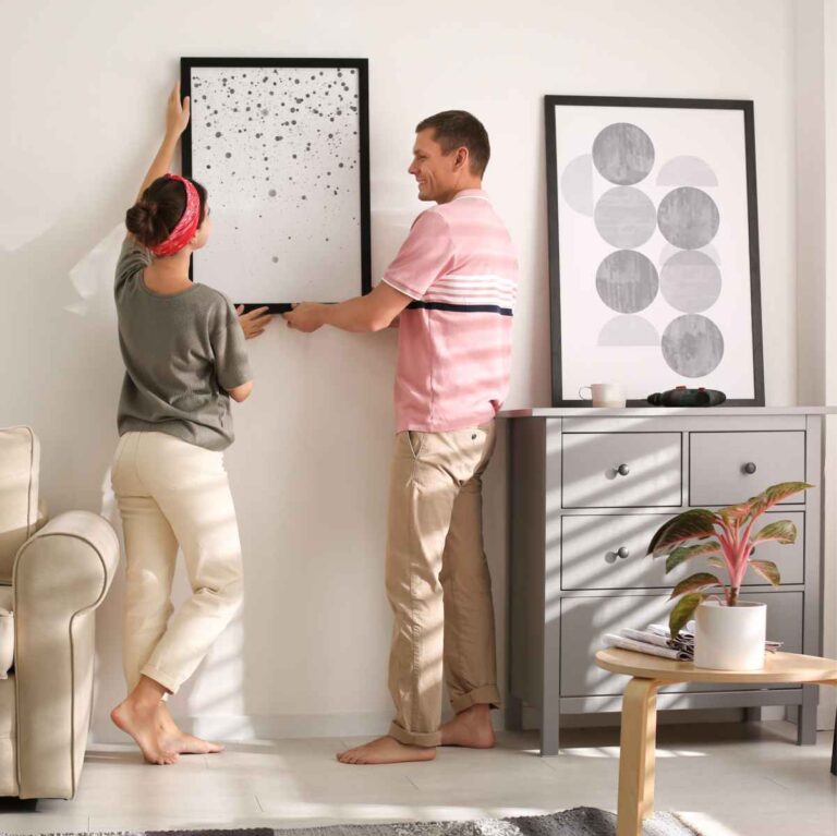 Un homme et une femme accrochent un tableau encadré au mur