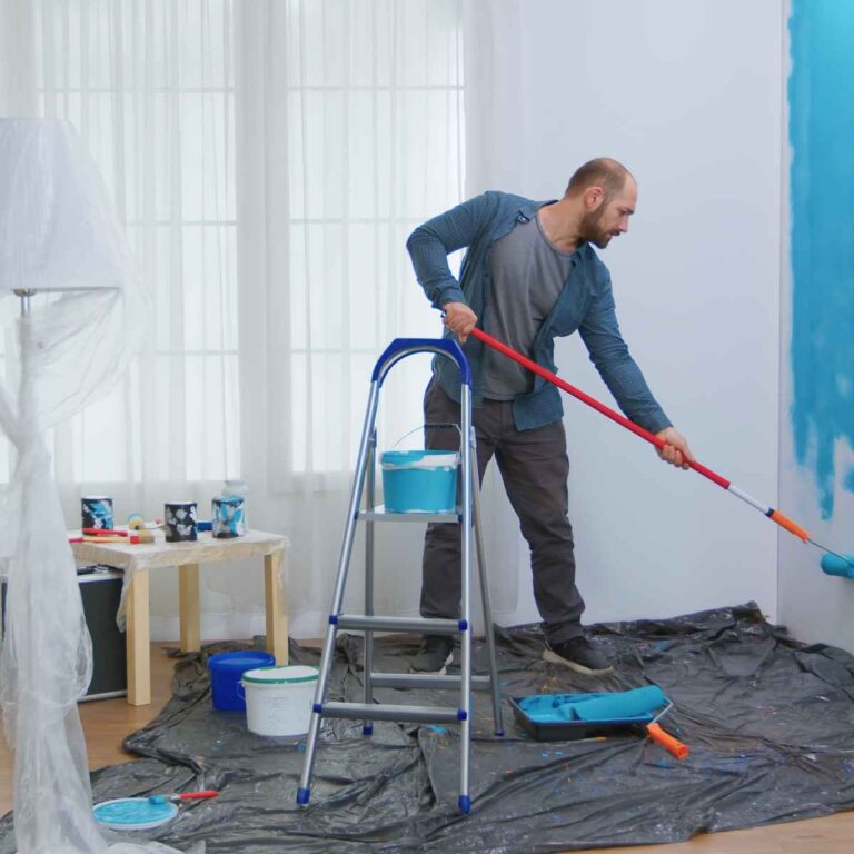 Un homme peint une pièce avec de la peinture bleue.