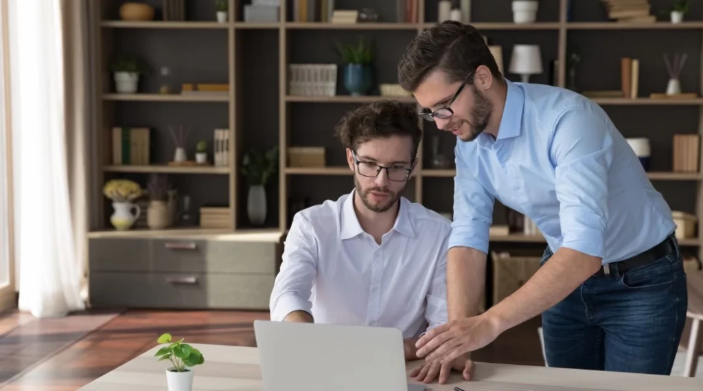 Two people talking while using a laptop